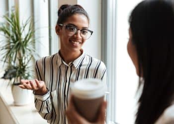 Duas mulheres conversando de forma amigável em ambiente de trabalho durante pausa para café.