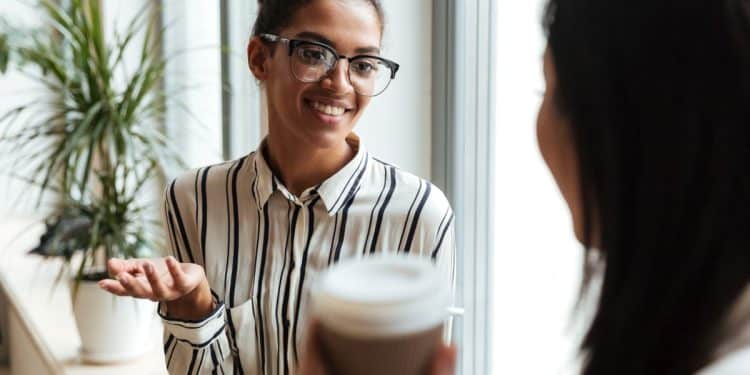 Duas mulheres conversando de forma amigável em ambiente de trabalho durante pausa para café.