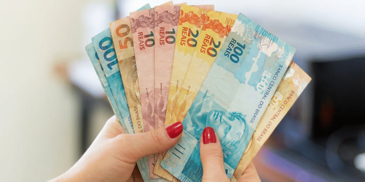 Mãos com unhas vermelhas exibem notas de 50, 10, 20 e 100 reais em formato de leque, mostrando a segunda família do real, simbolizando o pagamento de R$ 4.116.