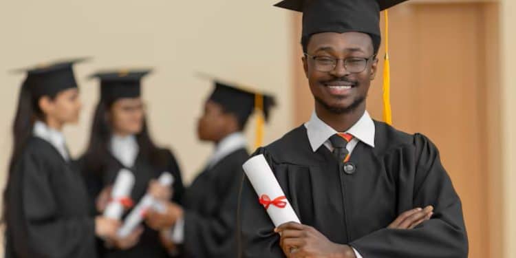 Jovem formando de beca e capelo sorri segurando o diploma