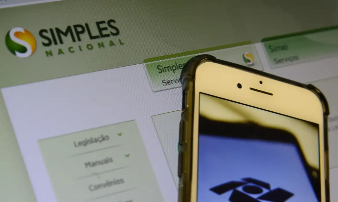 Tela de computador exibindo portal do Simples Nacional com smartphone em primeiro plano mostrando logo da Receita Federal