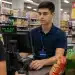 Jovem atendente de loja e mercado operando caixa durante atendimento a cliente em supermercado.