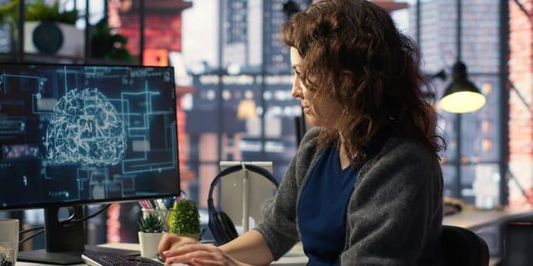 Mulher de cabelos cacheados digita em teclado observando cérebro holográfico com sigla AI na tela do monitor, simbolizando as profissões que mais podem crescer com a inteligência artificial.
