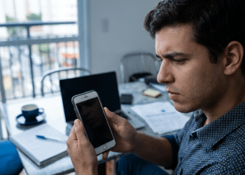 Homem observa o celular com expressão preocupada