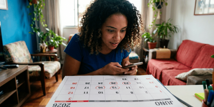Mulher consulta o celular diante de um calendário de junho de 2026 sobre a mesa