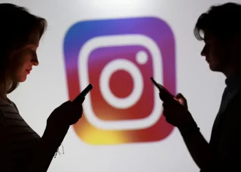 Silhuetas de uma mulher e um homem usando smartphones em frente ao logotipo colorido do Instagram, representação dos recursos de segurança ampliados pela Meta para usuários menores de idade.