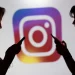 Silhuetas de uma mulher e um homem usando smartphones em frente ao logotipo colorido do Instagram, representação dos recursos de segurança ampliados pela Meta para usuários menores de idade.