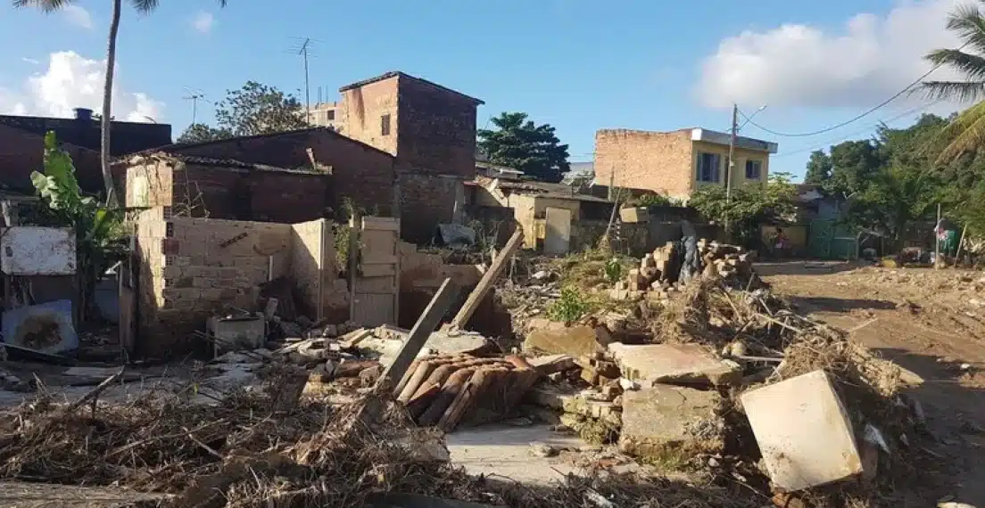 Área residencial com entulhos e casas danificadas após desastre, representando o próximo repasse do Auxílio Reconstrução.