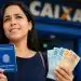 Mulher segurando carteira de trabalho e notas de reais em frente à Caixa, em referência ao saque-aniversário do FGTS 2026.