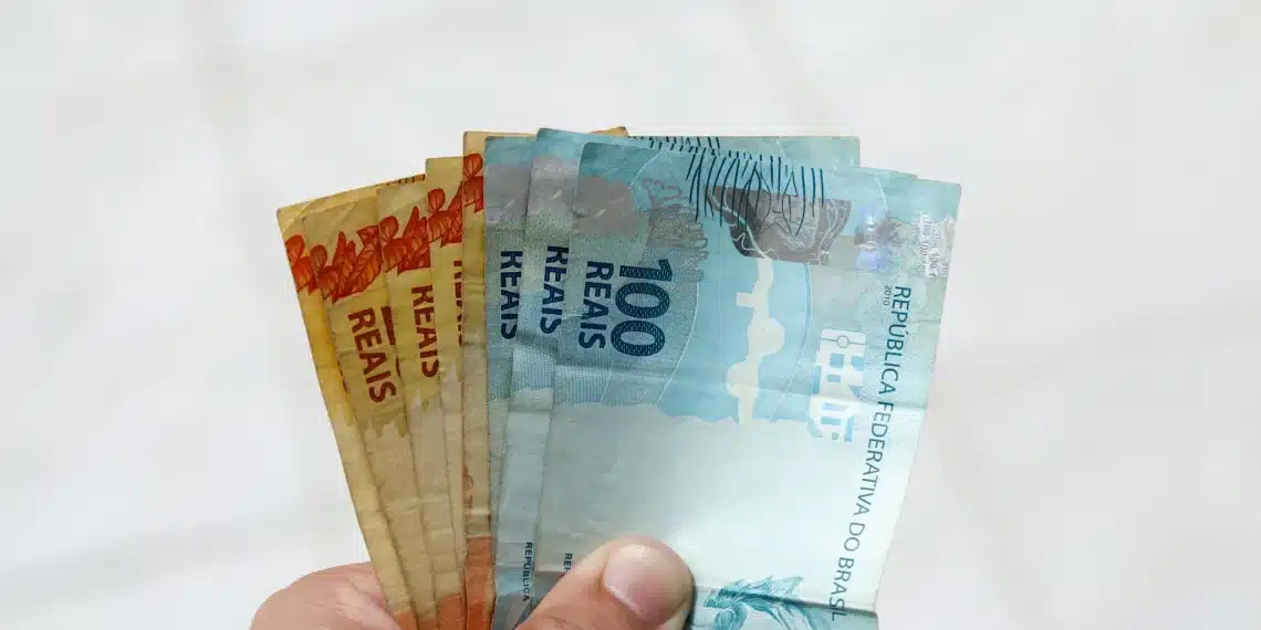 Mão segurando notas de reais para ilustrar pagamento do Abono Salarial PIS/Pasep 2025