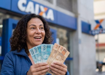 Mulher segura cédulas de R$ 50 e R$ 100 em frente a uma agência da Caixa, em referência ao Saque Calamidade do FGTS em Goiana.