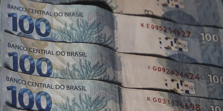 Cédulas de R$ 100 do Banco Central do Brasil empilhadas em leque mostrando números de série, simbolizando o pagamento da segunda parcela do 13º salário do INSS.