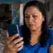 Mulher consultando o celular em uma casa danificada, representando a solicitação do Saque Calamidade pelo app FGTS.