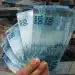 Trabalhador segurando notas de R$ 100, representando os 3 pagamentos extras para CLT em 2026