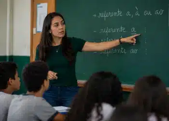 Professora apontando para quadro com explicação sobre o uso correto de referente a, à ou ao durante aula de português.