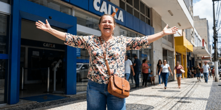 Mulher comemora em frente à Caixa Econômica após benefício liberado.