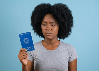 Jovem negra com expressão preocupada segura carteira de trabalho.
