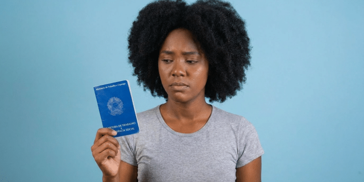 Jovem negra com expressão preocupada segura carteira de trabalho.