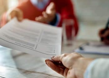 Entrevista de emprego com entrega de currículo em ambiente formal.