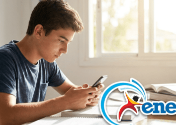 Jovem concentrado consulta celular ao lado de materiais de estudo e logo do Enem.
