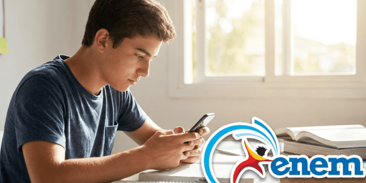 Jovem concentrado consulta celular ao lado de materiais de estudo e logo do Enem.