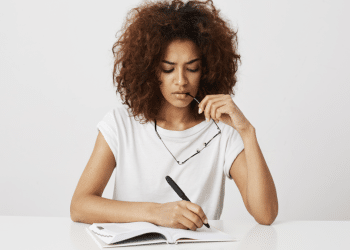 Jovem mulher refletindo enquanto escreve em caderno branco minimalista.