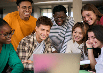 Jovens sorrindo e olhando juntos para um notebook em ambiente moderno.