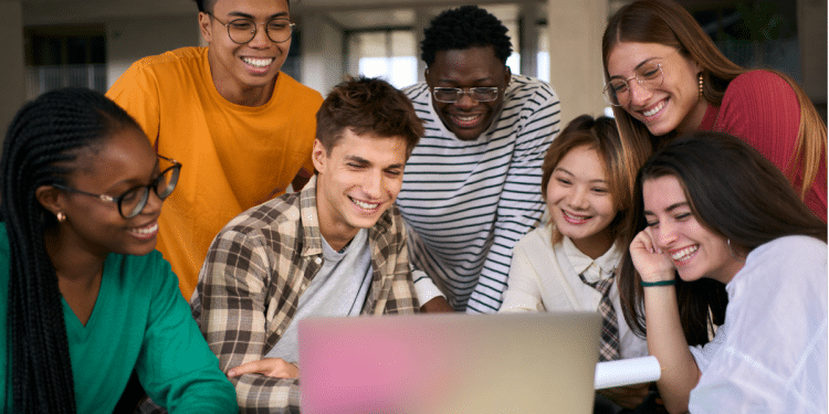 Jovens sorrindo e olhando juntos para um notebook em ambiente moderno.