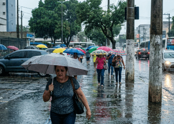 Pedestres atravessam avenida movimentada sob forte chuva em cidade brasileira.