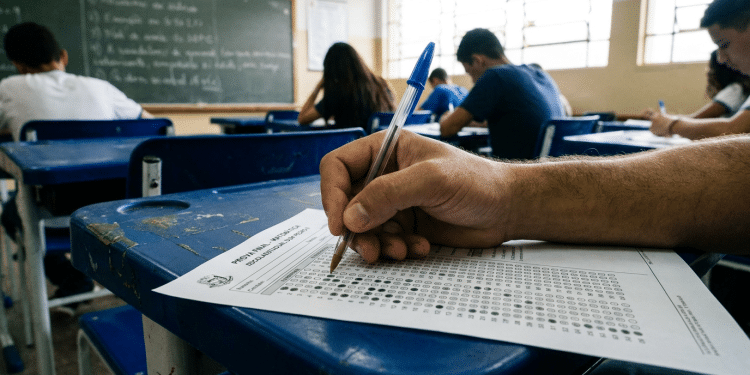Mão masculina marcando gabarito de prova em sala de aula.