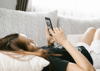 Mulher deitada em sofá enquanto mexe em celular.