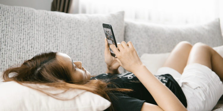 Mulher deitada em sofá enquanto mexe em celular.