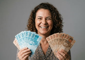 Mulher sorridente exibe notas de real em clima de conquista financeira.