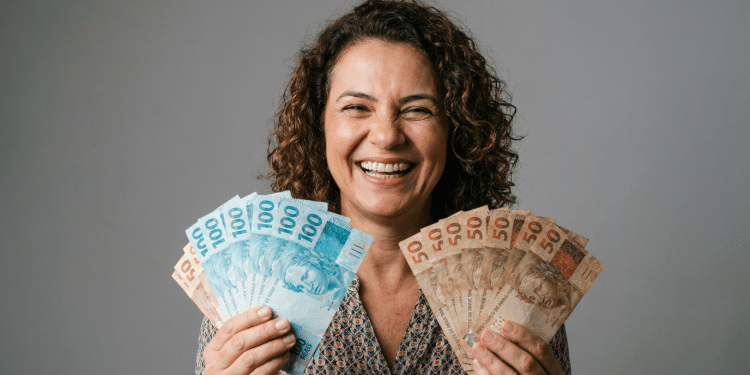 Mulher sorridente exibe notas de real em clima de conquista financeira.