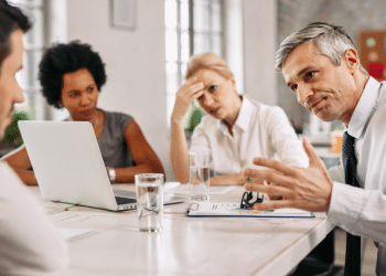 Equipe discute soluções em reunião corporativa com tensão aparente.