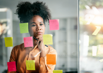 Jovem analisa ideias em mural de post-its coloridos no escritório.