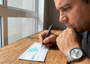 Homem pensativo preenche cheque da Caixa Econômica Federal.