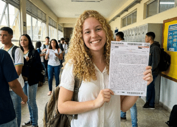 Jovem sorridente exibe folha de redação do Enem em escola.