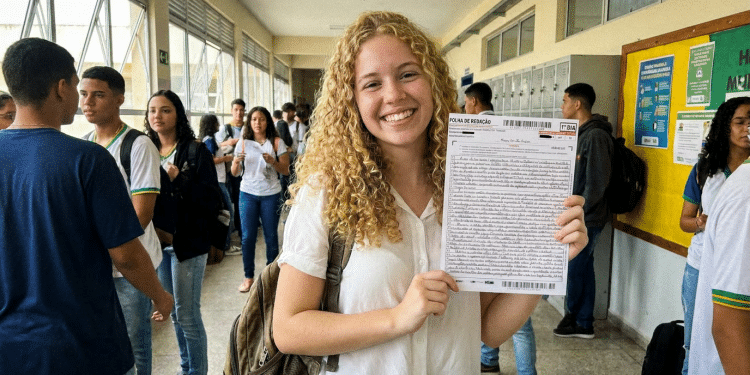 Jovem sorridente exibe folha de redação do Enem em escola.