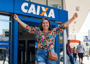 Mulher celebra saque na Caixa Econômica Federal em frente à agência.