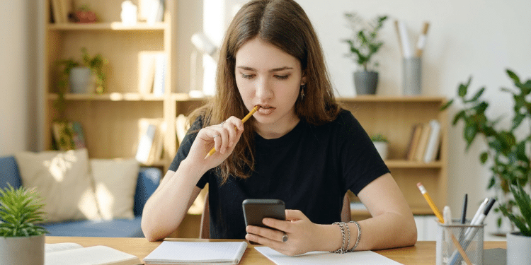 Estudante concentrada usando celular para estudo em ambiente doméstico.