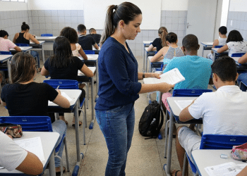 Mulher distribuindo prova em sala de aula.