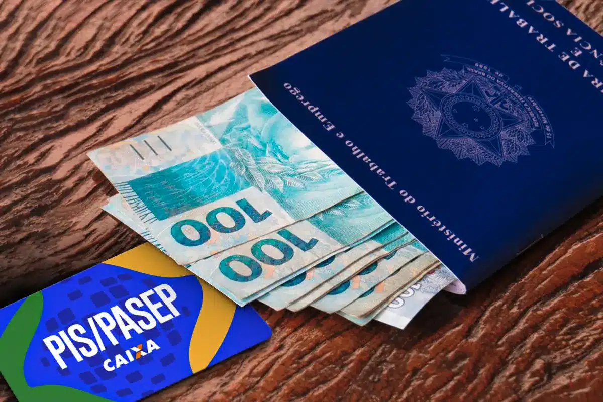 Carteira de trabalho com notas de cem reais e cartão do PIS/Pasep da Caixa, símbolos do Abono Salarial e do ressarcimento.