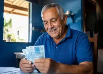Homem idoso sorrindo ao contar notas de dinheiro, representando o adicional de 50% no INSS em junho de 2026
