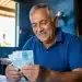 Homem idoso sorrindo ao contar notas de dinheiro, representando o adicional de 50% no INSS em junho de 2026