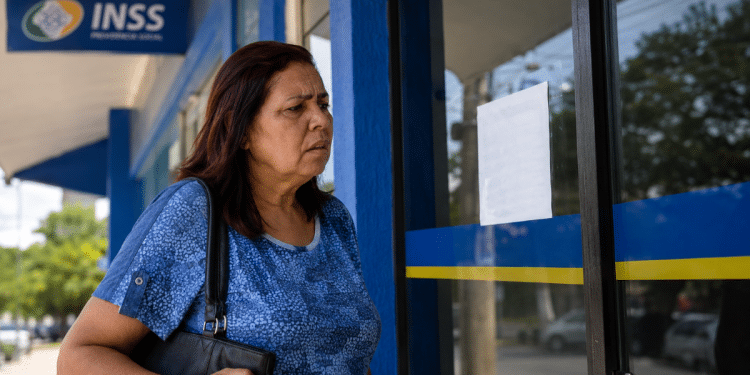 Mulher observa porta fechada de agência do INSS com expressão preocupada na calçada