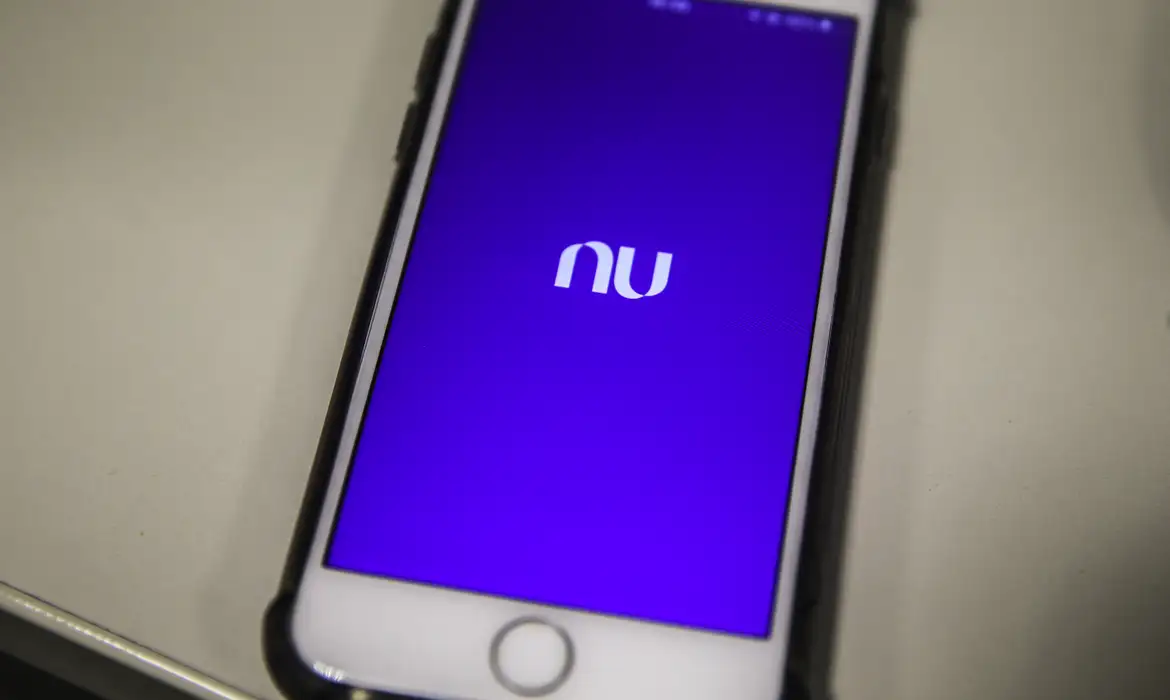 Smartphone sobre a mesa exibe a tela inicial do aplicativo do Nubank, onde fica o Monitoramento de CPF
