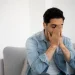 Homem em ambiente doméstico demonstrando sinais de ansiedade e tensão emocional ao cobrir o rosto com as mãos.