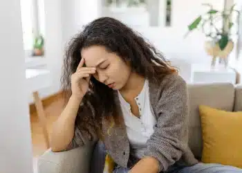 Mulher sentada no sofá com expressão preocupada, representando ansiedade, insegurança e dúvidas sobre si mesma.