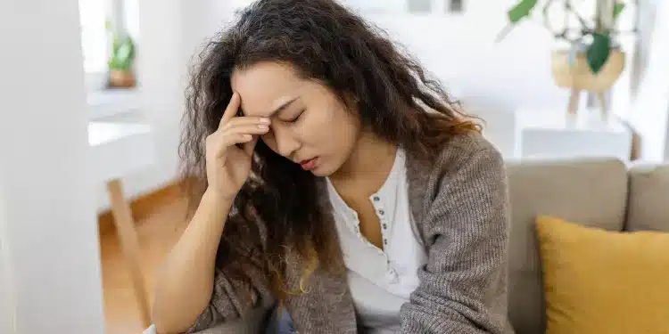Mulher sentada no sofá com expressão preocupada, representando ansiedade, insegurança e dúvidas sobre si mesma.